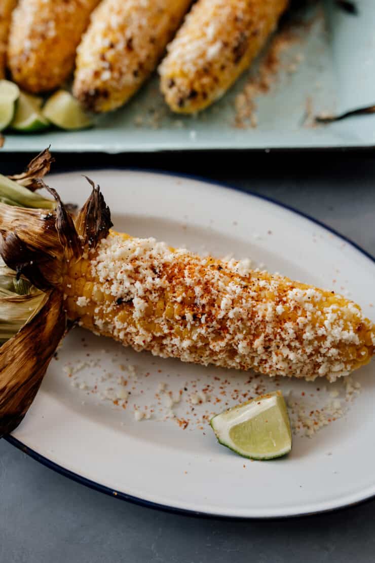 one cob of mexican street corn on an oblong white dish with a lime wedge