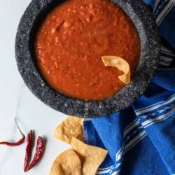 overhead shot of a bowl of chile de arbol spicy salsa with a chip sticking out of it