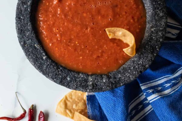 overhead shot of a bowl of chile de arbol spicy salsa with a chip sticking out of it