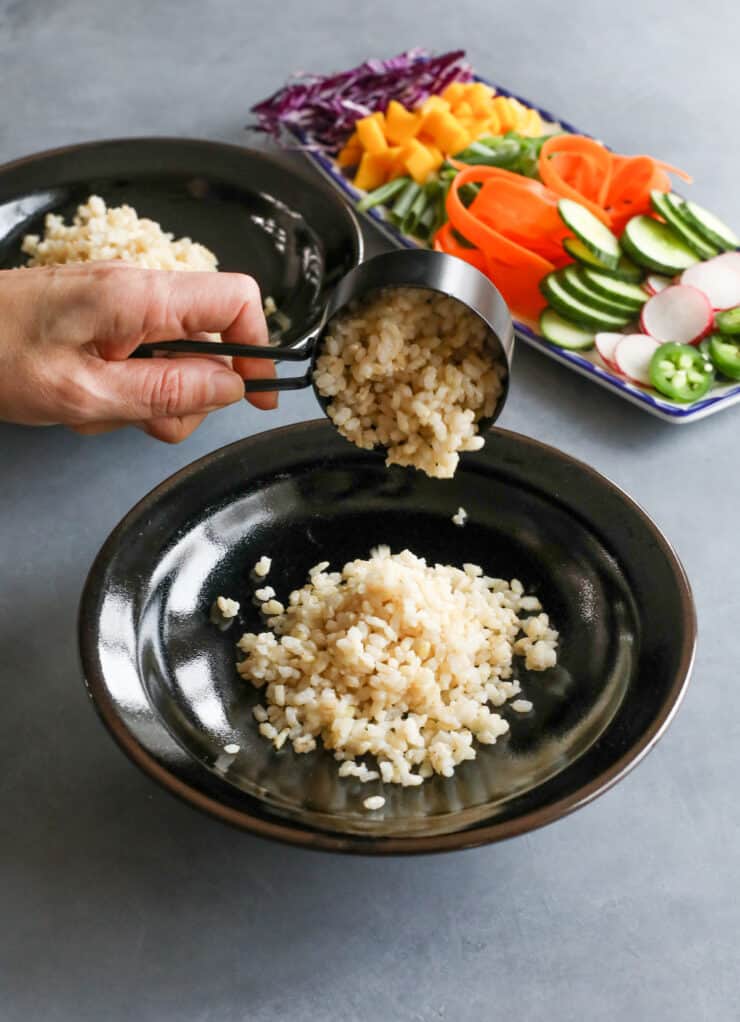 hand measuring brown rice into a black bowl 
