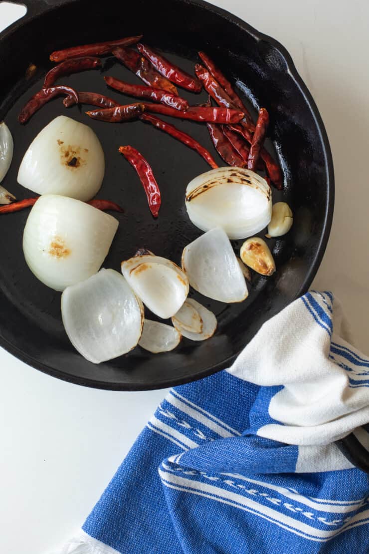 onion quarters and garlic cloves added to skillet with chiles de arbol