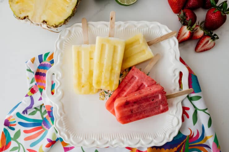 three pineapple paletas and two strawberry paletas on a vintage platter and colorful Otomi fabric