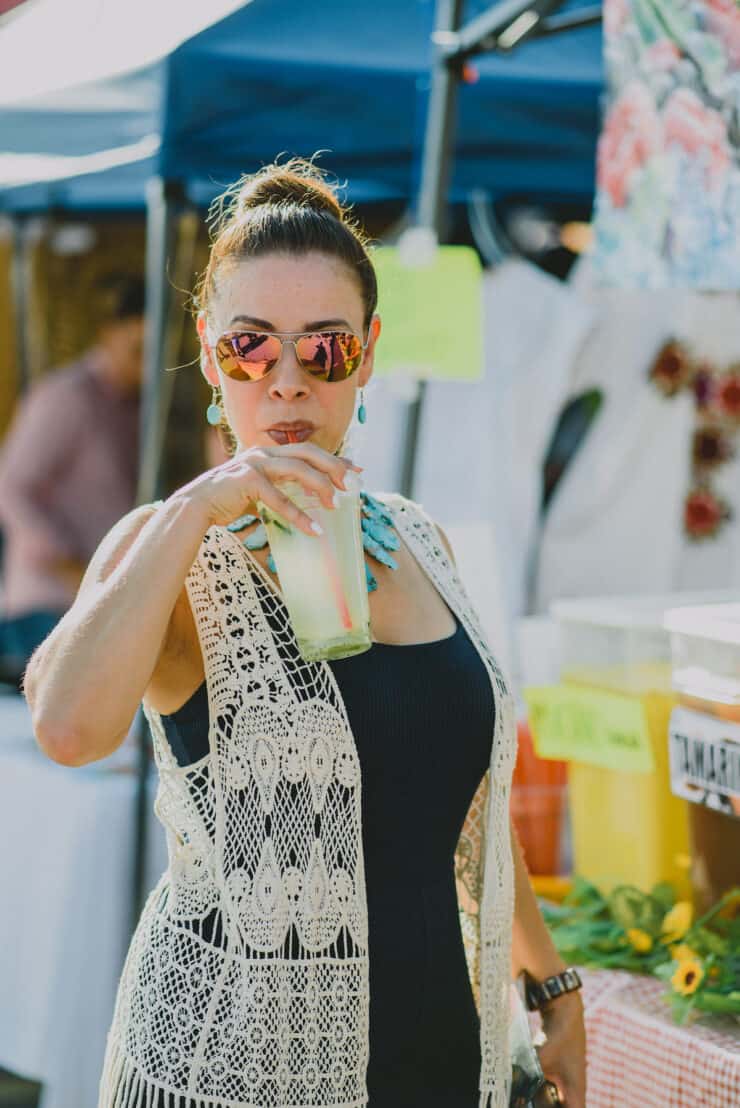 latina blogger Yvette Marquez drinking a glass of agua de pepino at the farmer's market