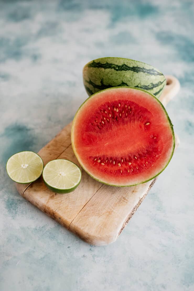 halved watermelon and halved lime on a wooden cutting board