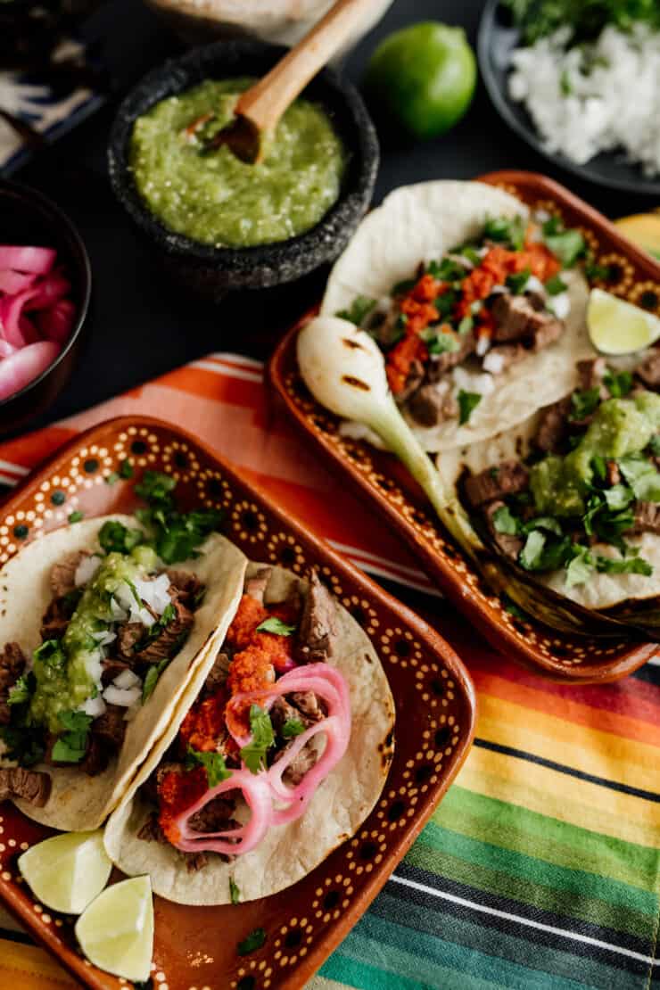 two square plates filled with carne asada tacos on a multicolored tablecloth