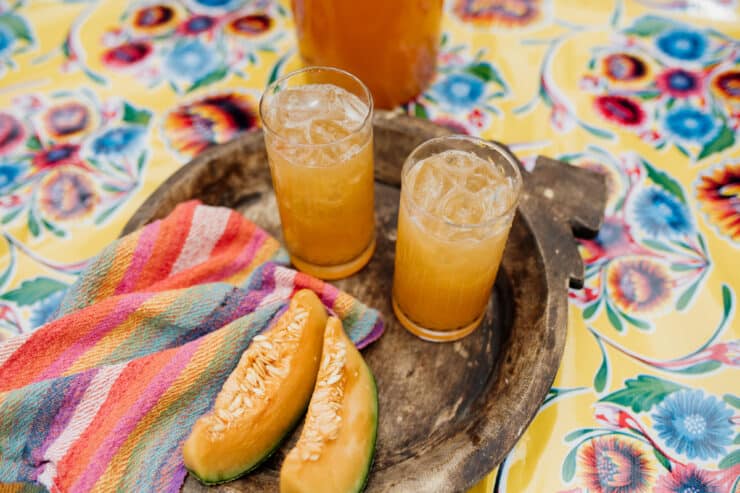 Agua de Melón (Melon Water) on a wooden tray with a striped colorful napkin and yellow floral Mexican tablecloth