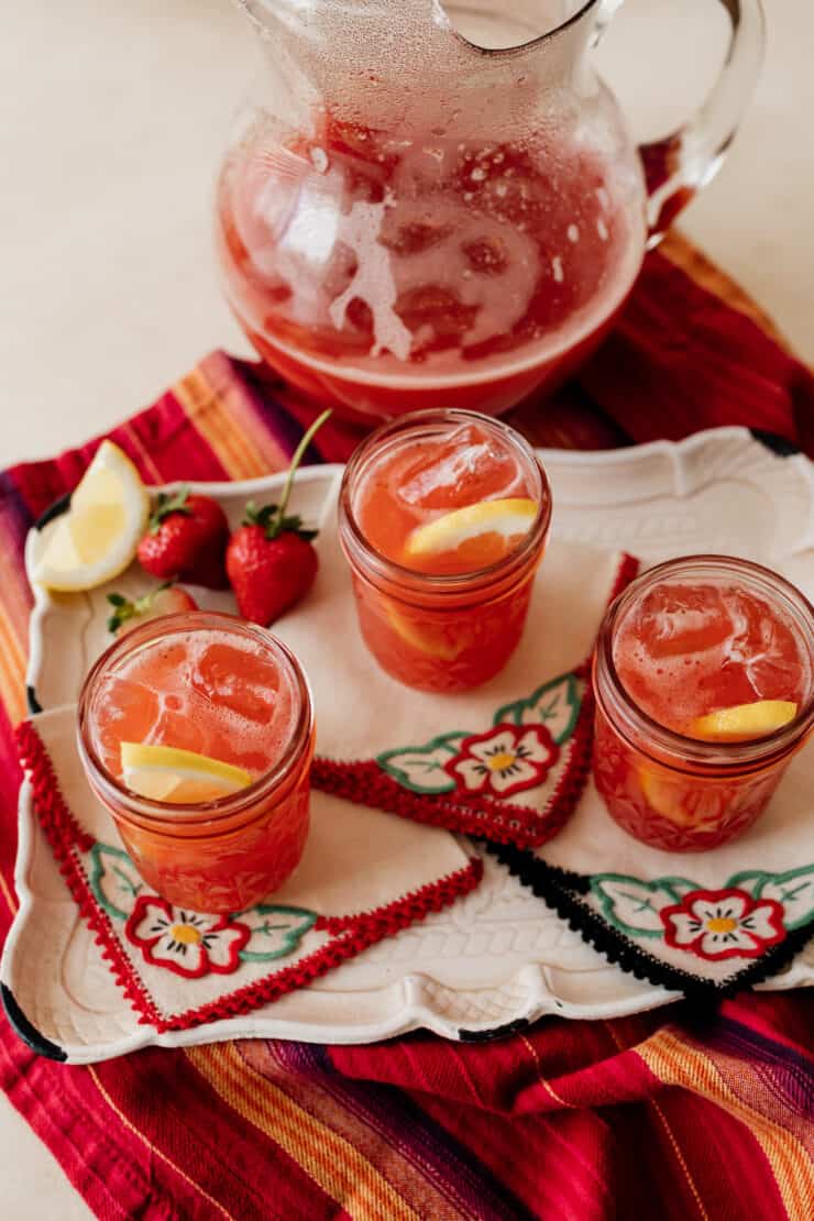 three mason jars of strawberry fruit tea with a pitcher of the sweet tea