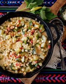 Calabacitas con Elote (Zucchini with Corn) topped with cheese on a board and colorful striped fabric