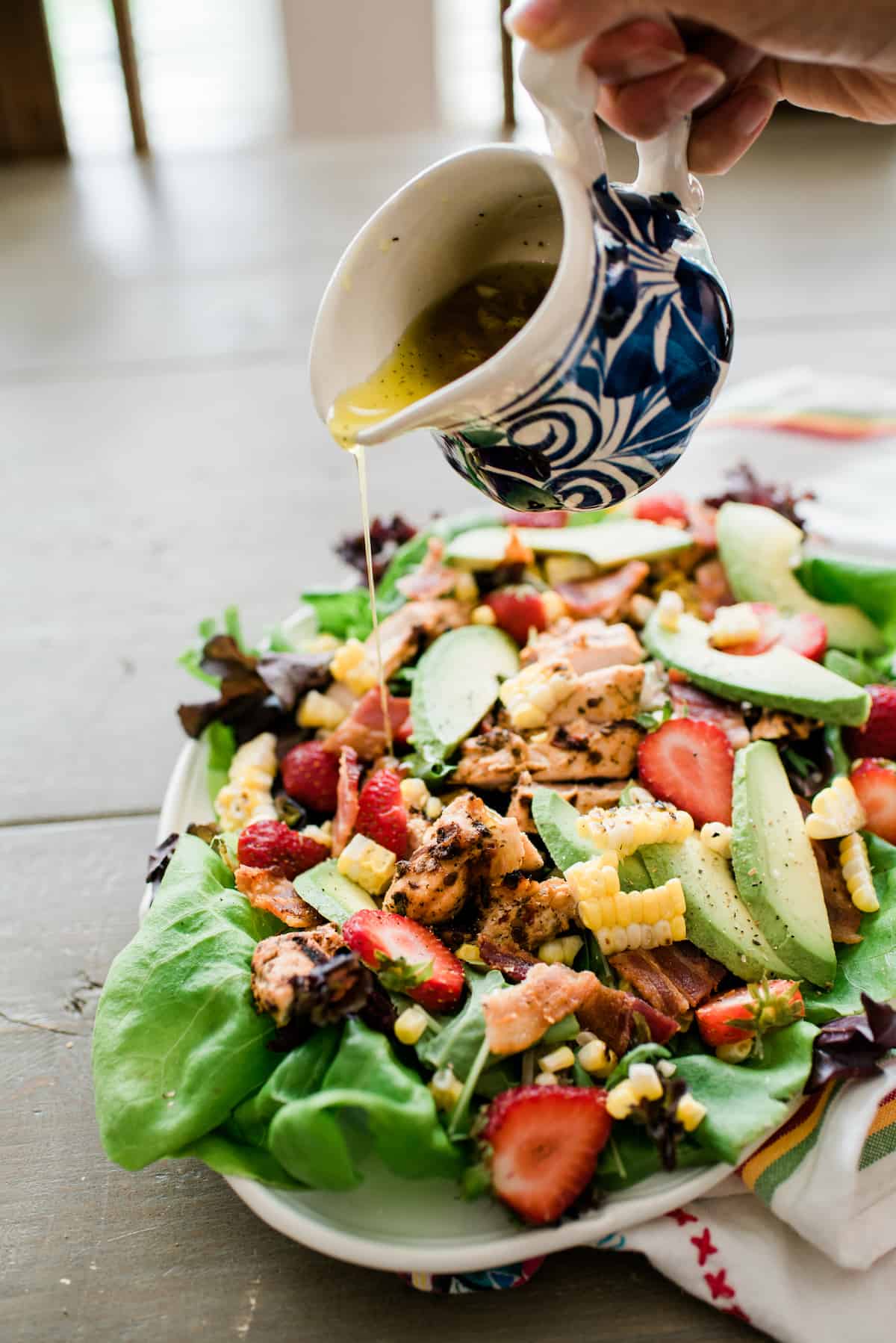 white and blue pitcher drizzling lemony vinaigrette over the summery cobb-ish salad with chipotle chicken and roasted corn