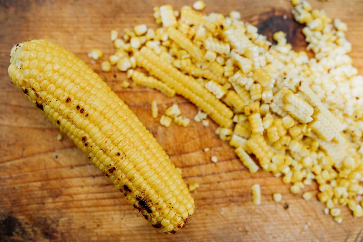 charred corn kernels and one corn on the cob roasted on a wooden cutting board