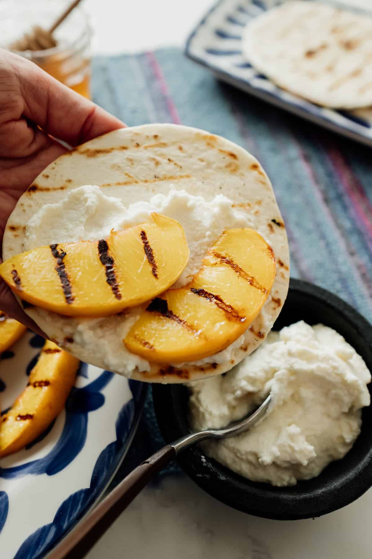 a hand holding a flour tortilla smothered with ricotta and grilled peaches. 