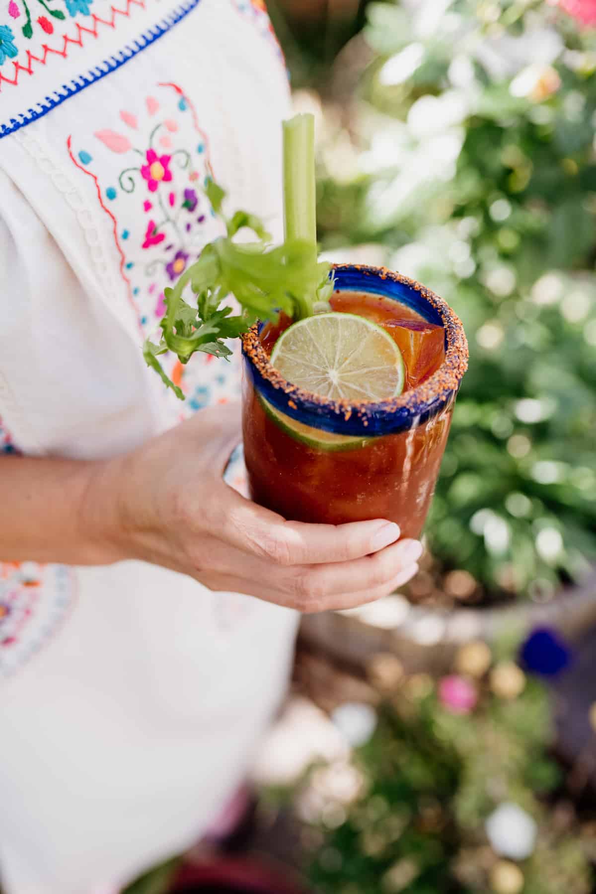 Mexican dress Latina holding a Spicy Michelada in a Mexican hand blown glass with a celery stalk and lime slice as garnish