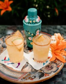 two glasses of melon margarita on a serving tray with a turquoise cocktail shaker and orange lily