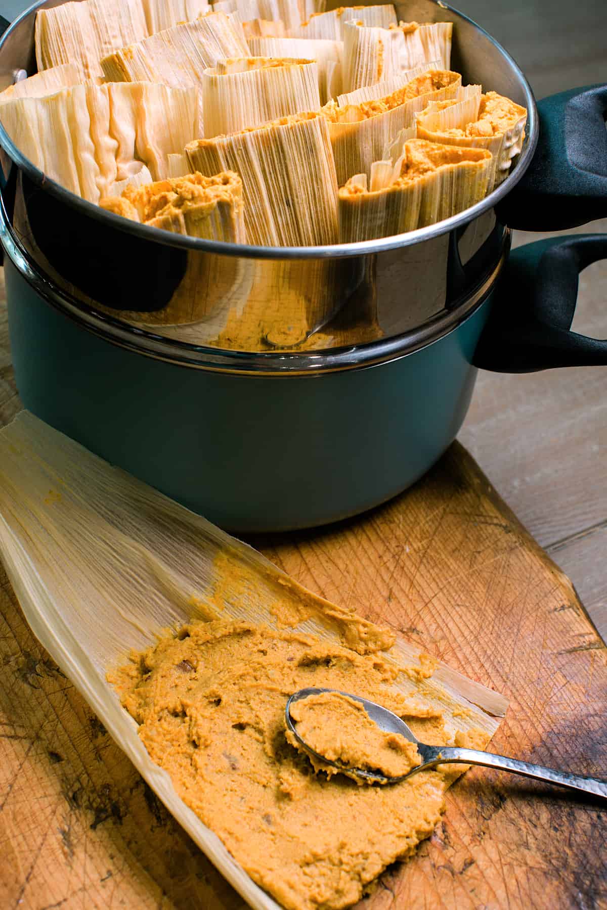 A steamer pot filled with prepared pumpkin tamales with one in the process of being filled in the forefront of the image