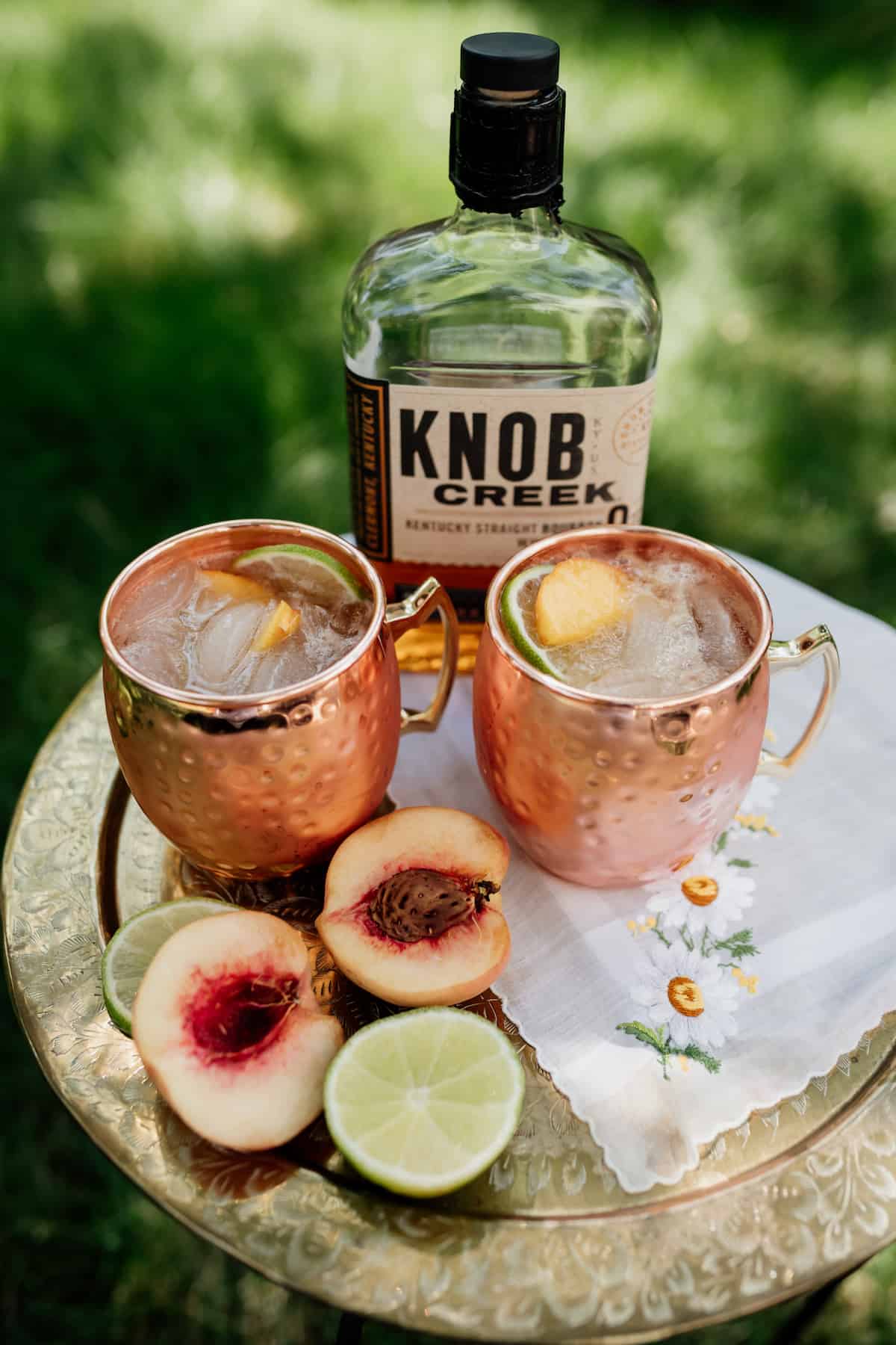 bottle of knob creek next to two peach kentucky mule cocktails
