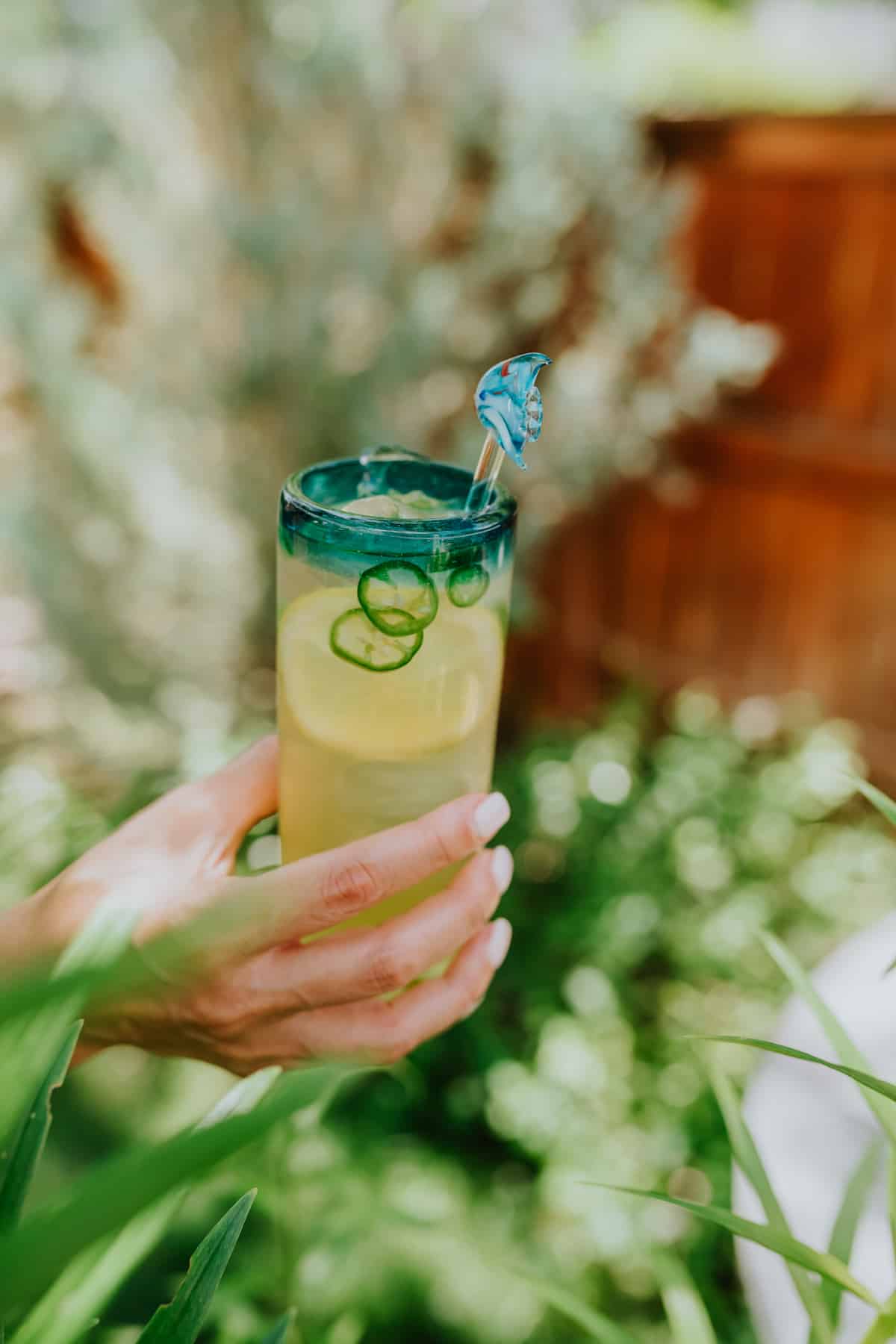 woman's hand holding a collins glass of green tea lemonade margarita with fresh sliced jalapeños and lemons