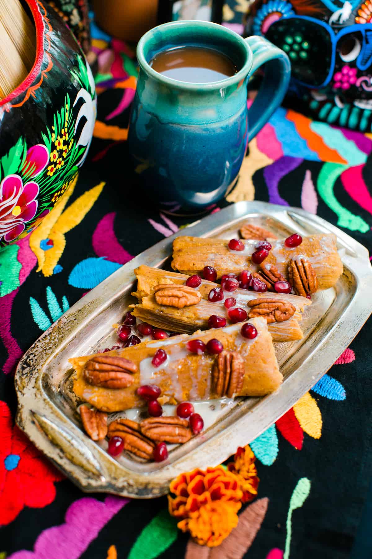 A festive platter of pumpkin spice tamales drizzled heavily with sweetened condensed milk and topped with pecan halves and pomegranate seeds for a Dia de los Muertos celebration