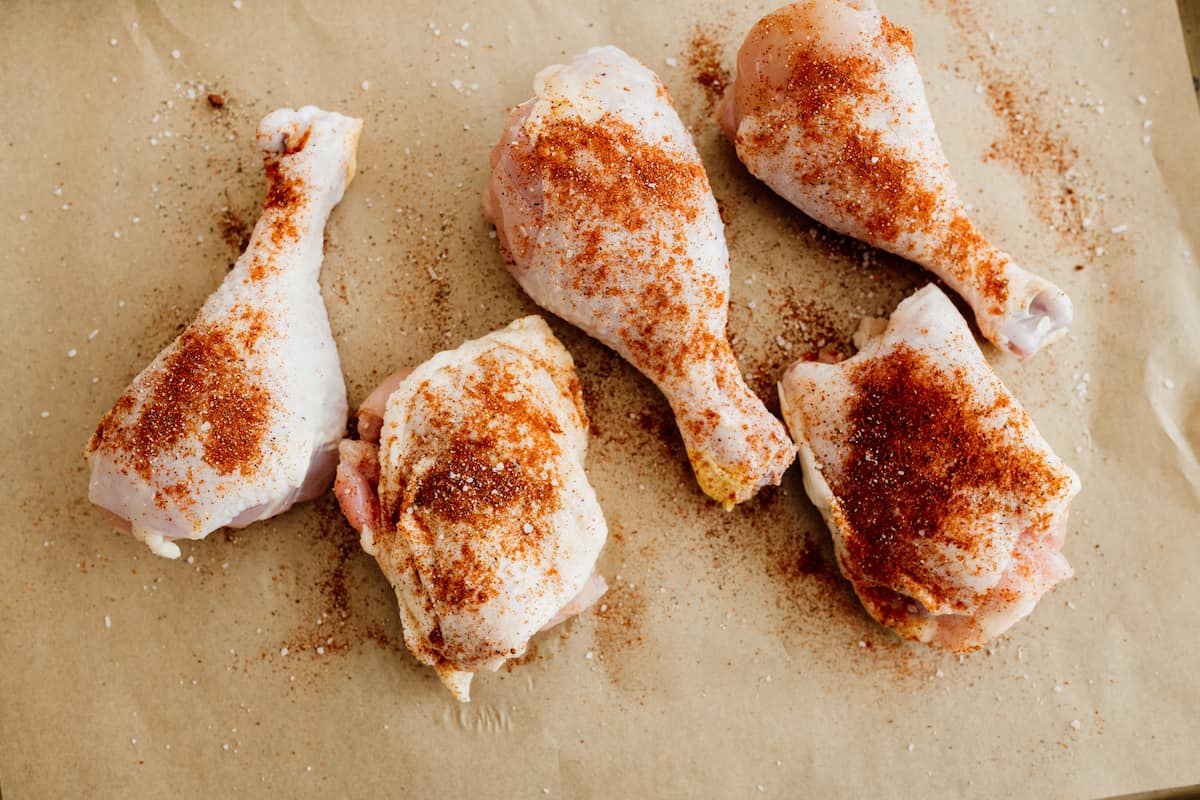 season chicken thighs and drumsticks on parchment paper