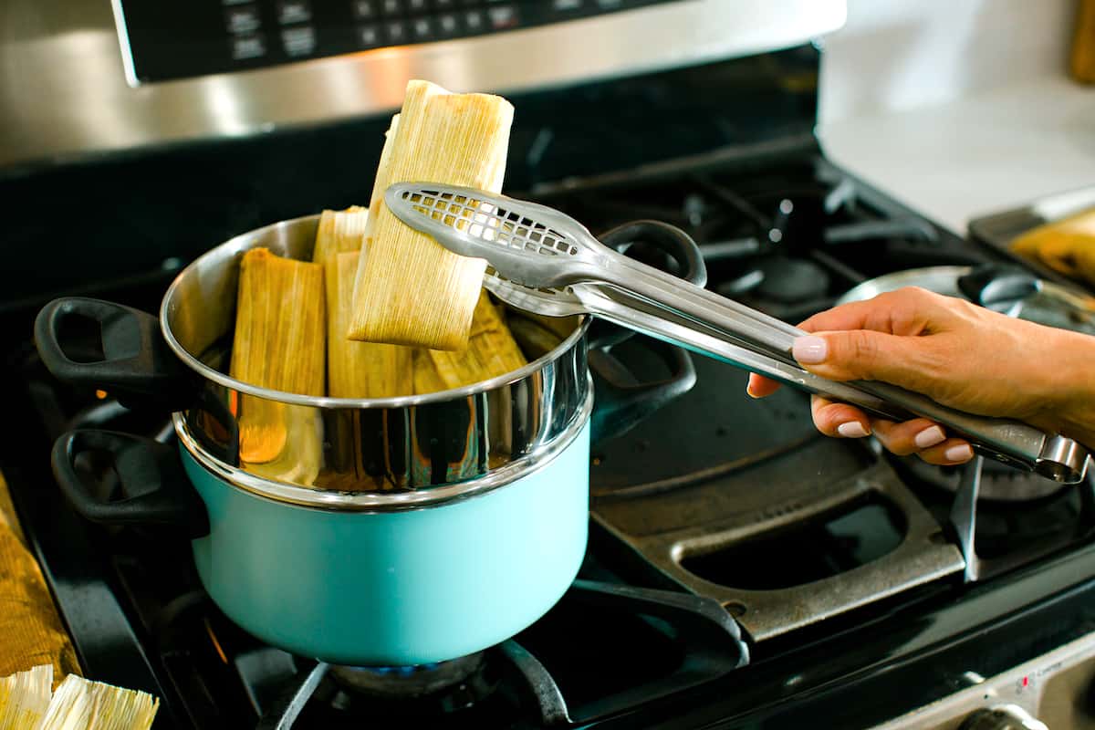 a chef removing hot steamed pumpkin spice tamales from a teal steamer pot