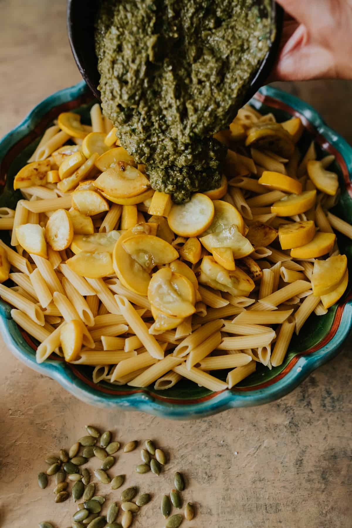 pouring cilantro pesto in a bowl or penne pasta