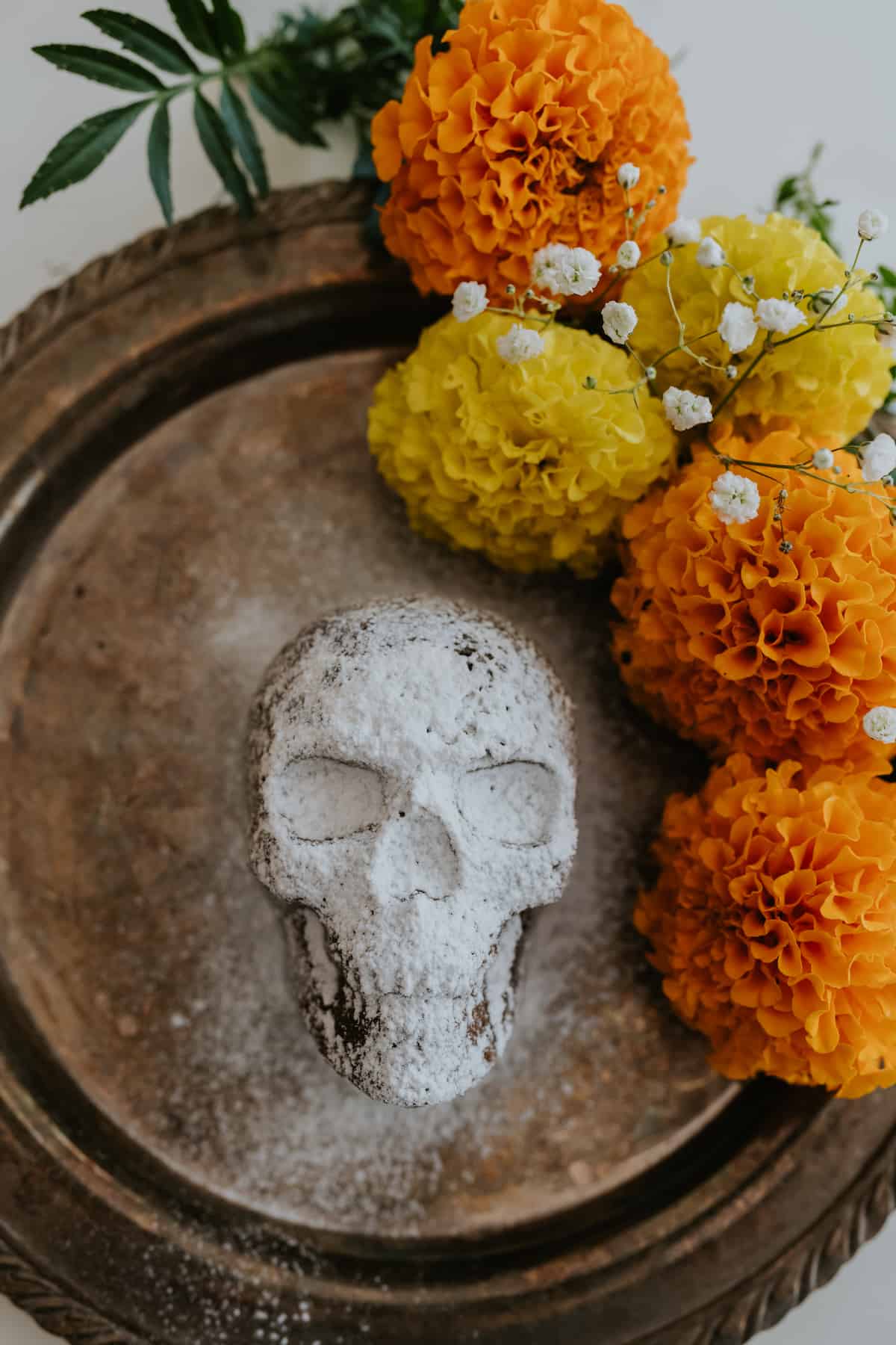 Decorates chocolate cake for Dia de los Muertos with powdered sugar and marigolds