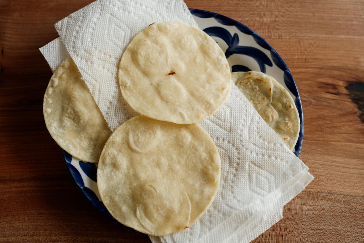 fried corn tortillas drained on paper towels on a blue and white plate