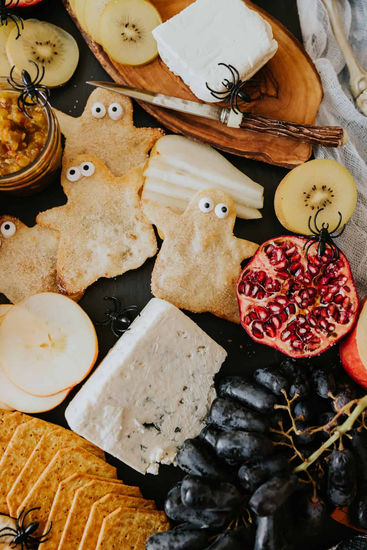 close up of bunuelo ghosts with candy eye balls surrounded by cheese and fresh fruit