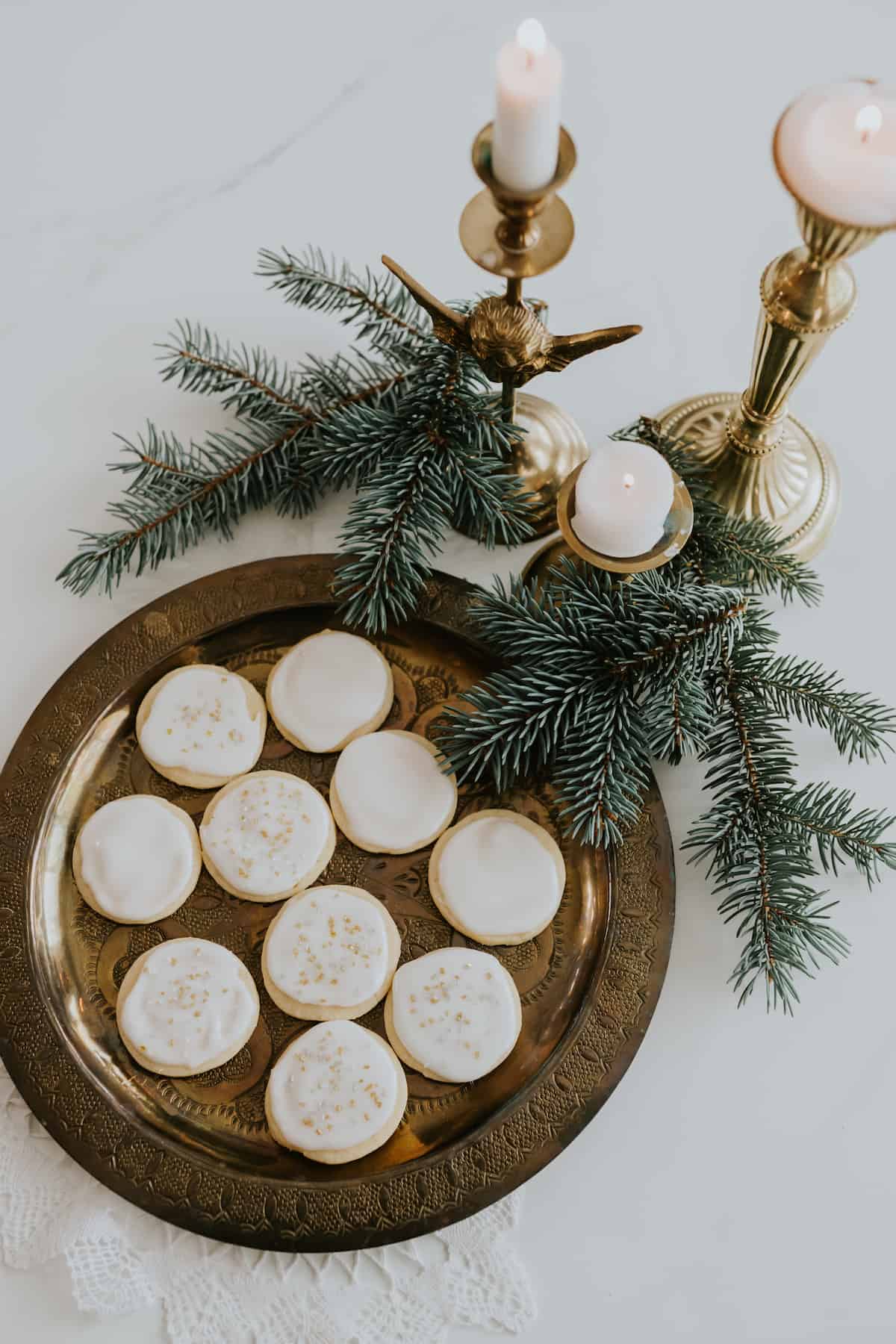 overhead shot of glazed lemon sugar cookies on a copper platter with a few sprigs of evergreen and a gold candelabra.
