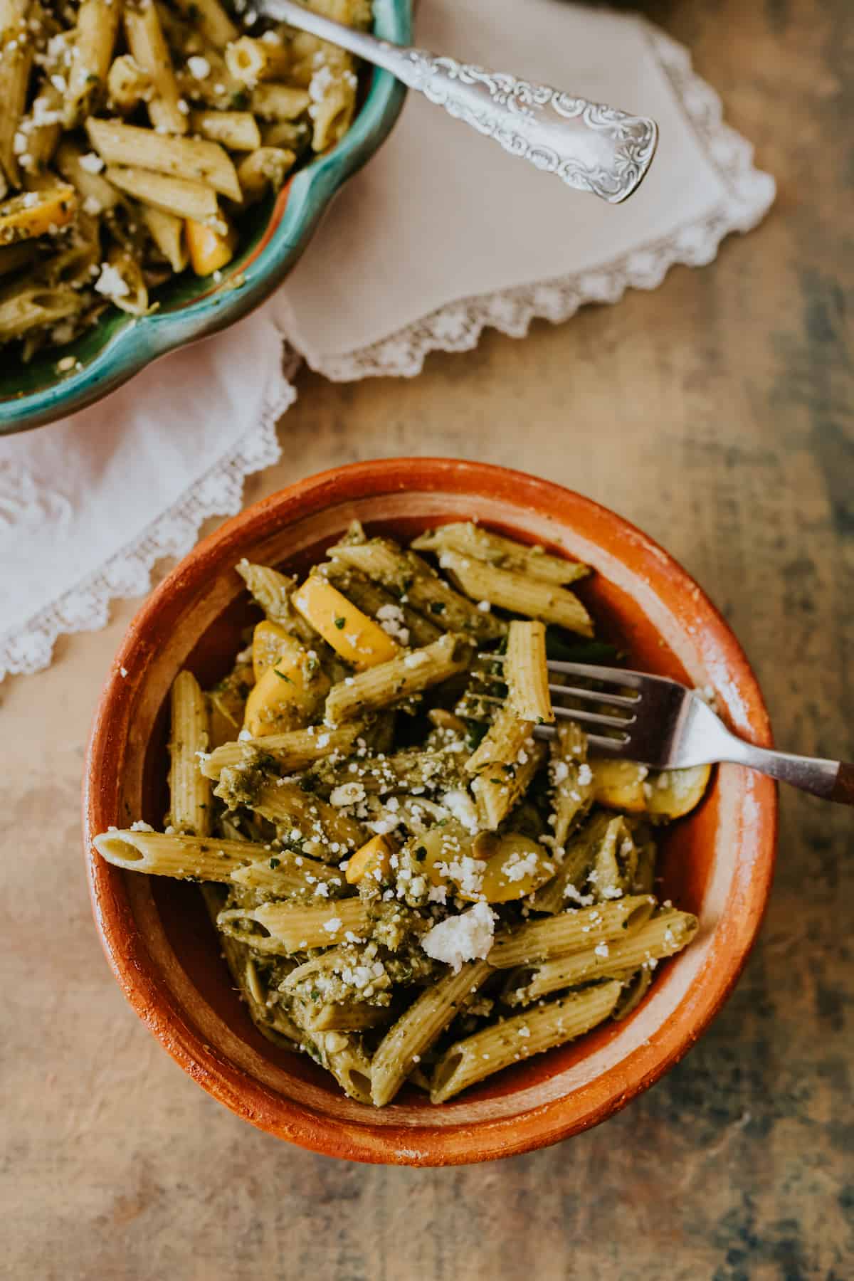 Spicy Cilantro Pesto Pasta in a brown bowl with fork and crumbled Cotija on rustic brown counter