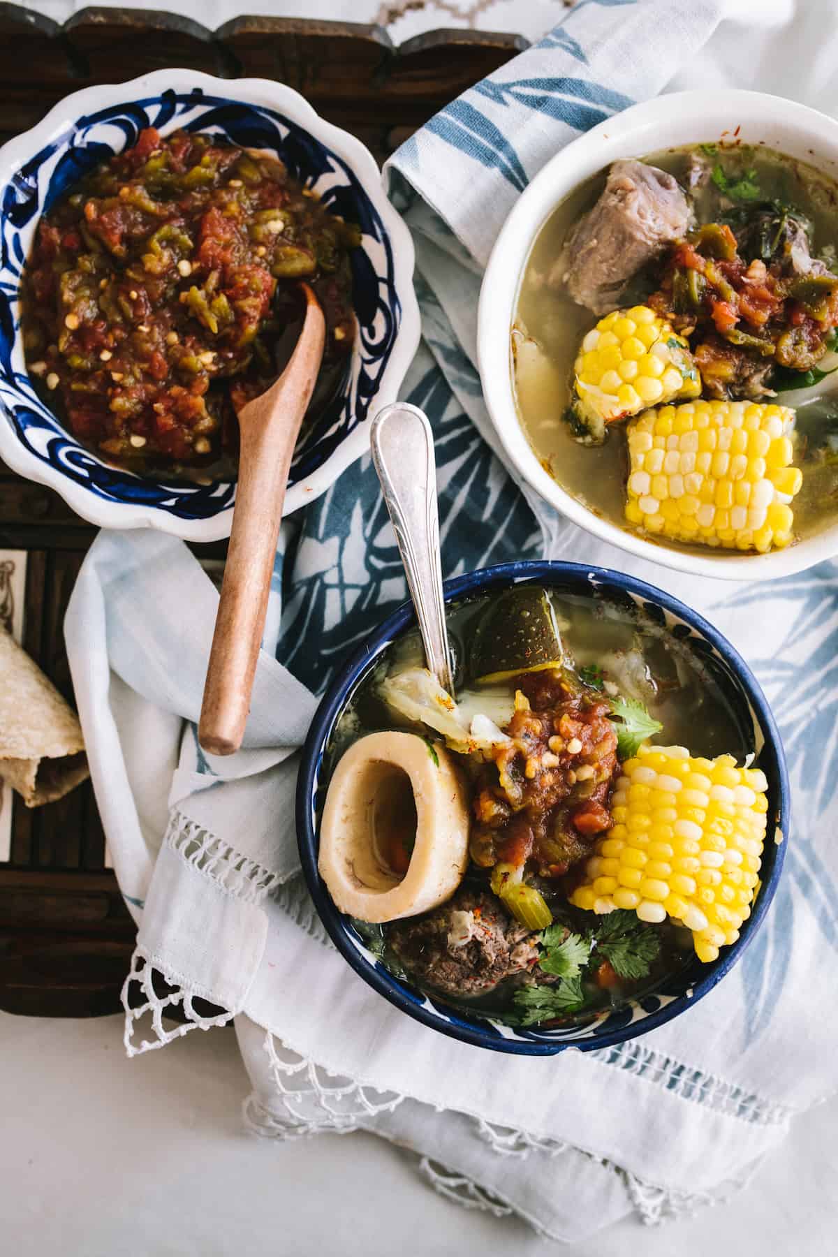 a blue and white serving bowl of homemade oxtail soup with corn tortillas and a bowl of salsa