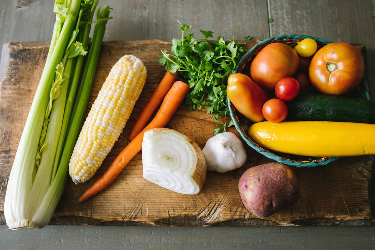 celery, corn, carrots, onion, potatoes, zucchini, tomatoes on a cutting board