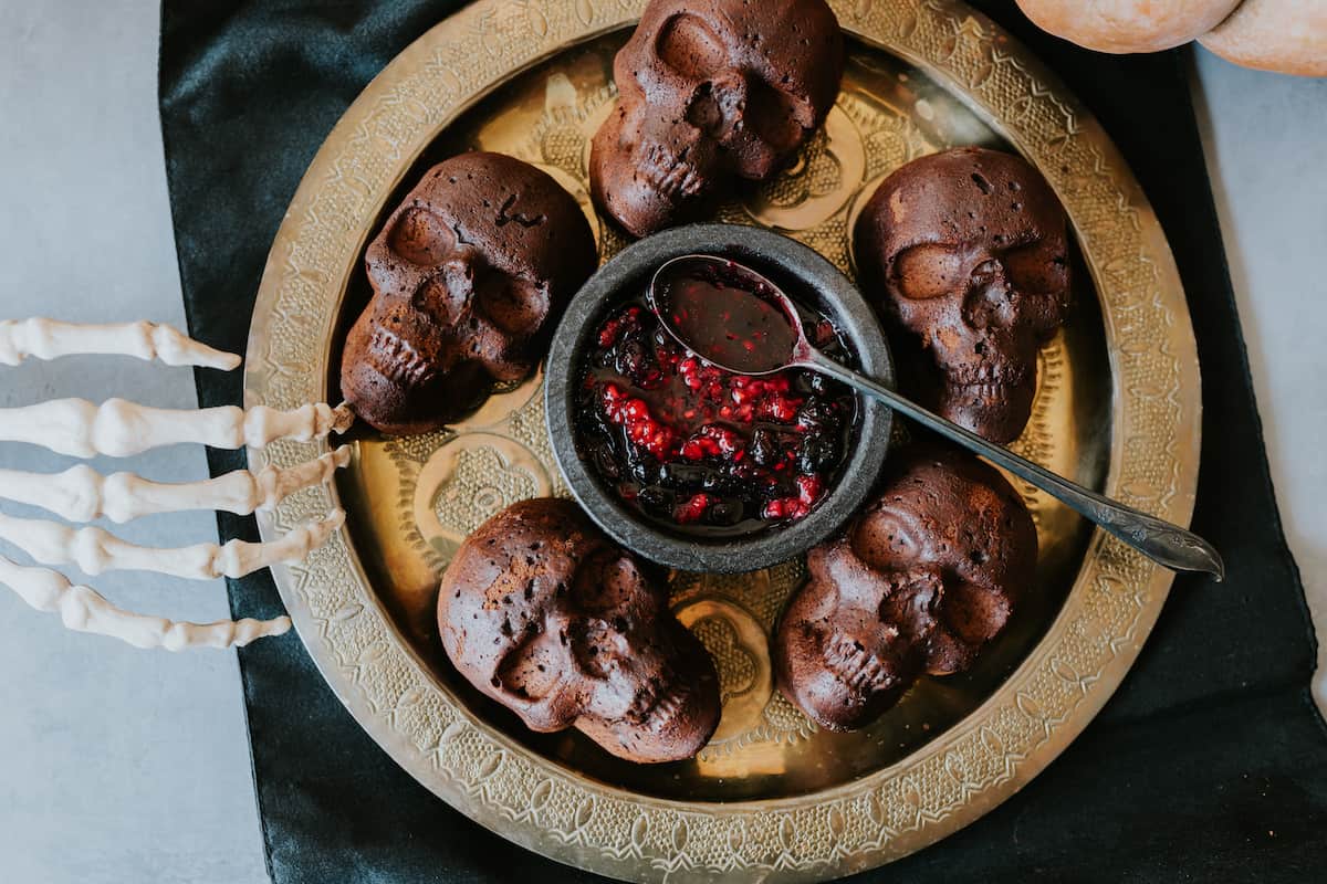 chocolate skulls cakes with a black bowl filled with roasted berry sauce on a gold vintage plate