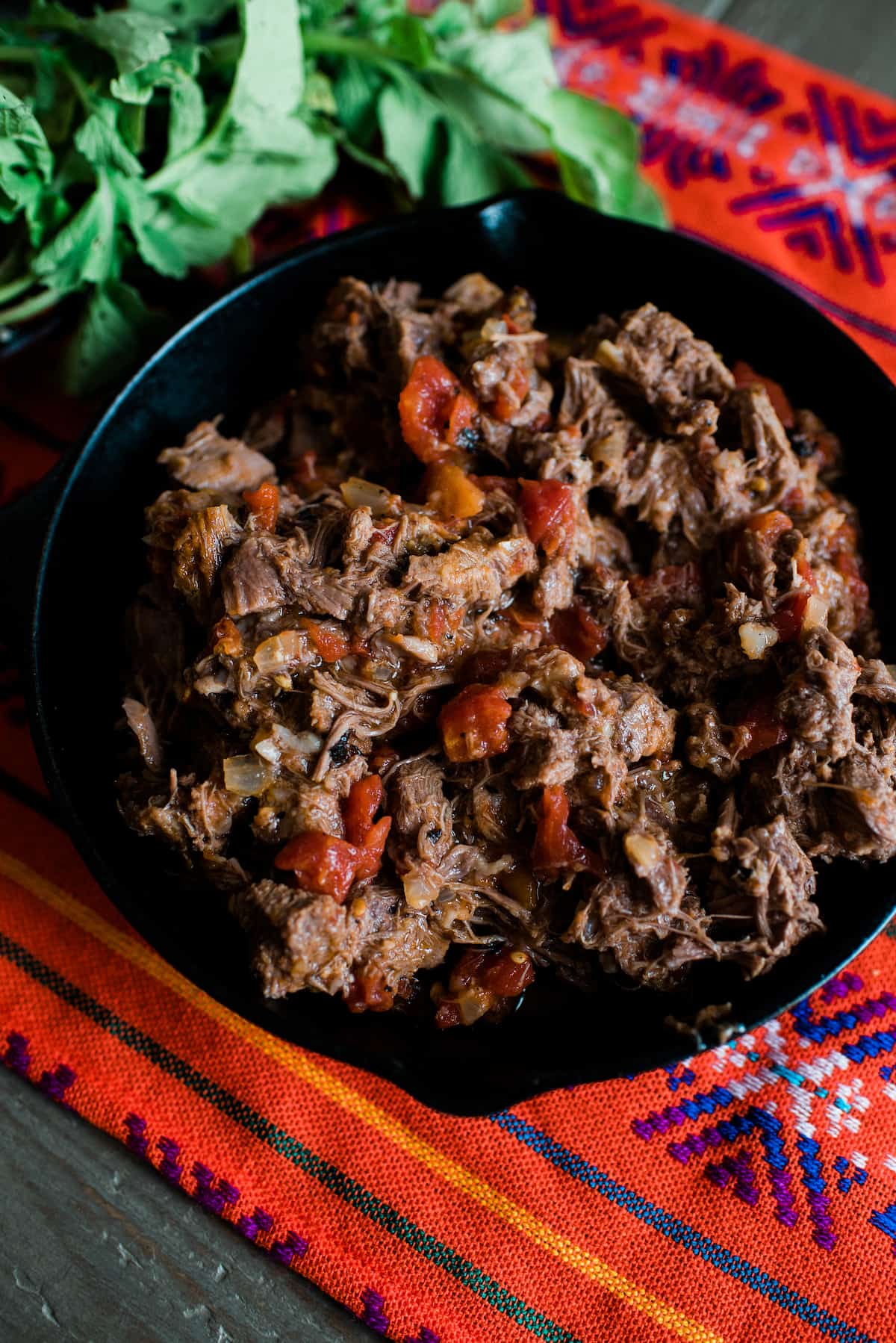 skillet filled with this slow cooker beef tongue recipe in a tomato sauce on a Mexican runner 