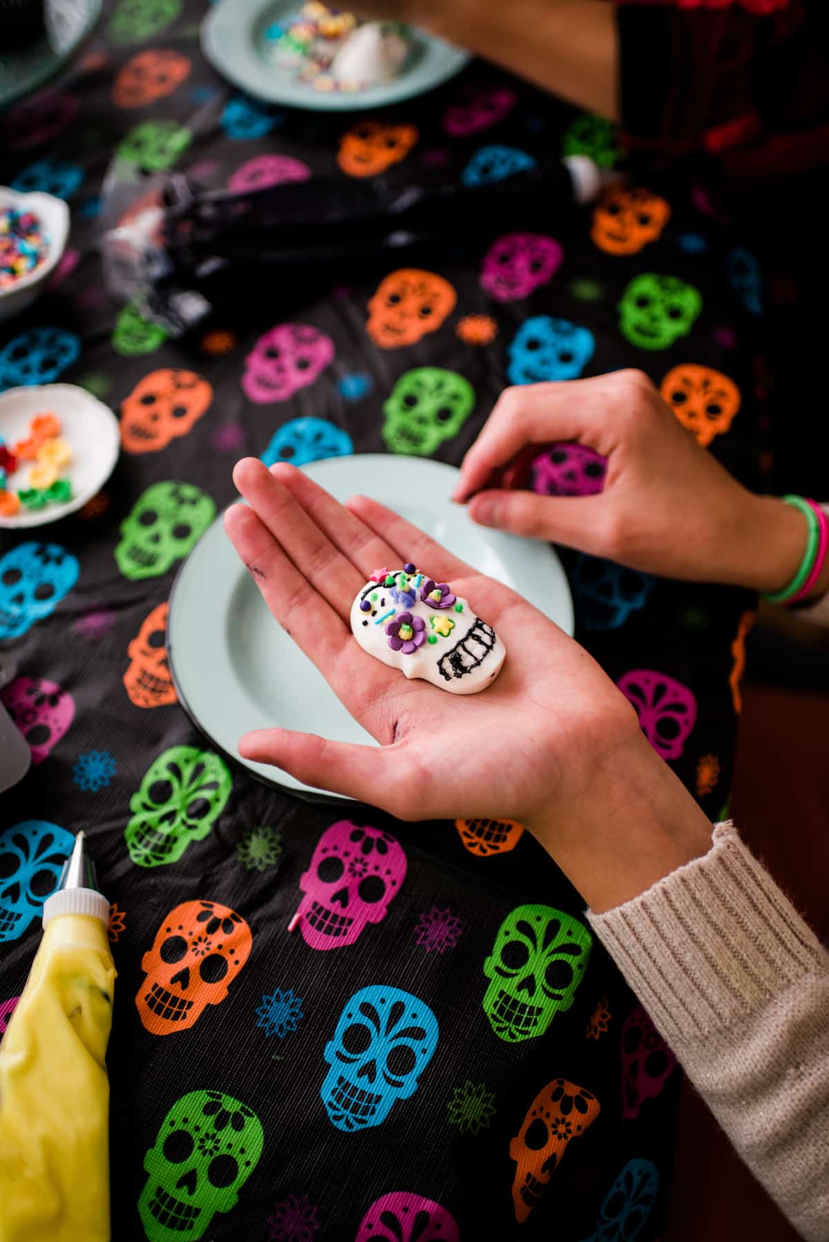 The author's children decorating their Dia de los Muertos candy skulls with colorful frosting, candy flowers, and sprinkles on top of a skull tablecloth 