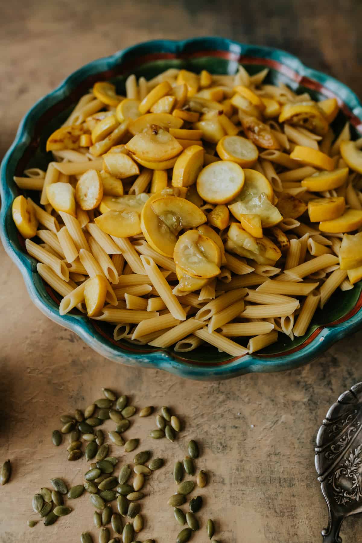 large bowl filled with cooked penne pasta topped with sautéed squash and pepitas on the table 