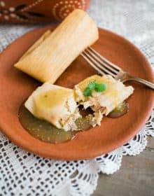 terracotta plate with chicken tamales verdes and a silver fork.