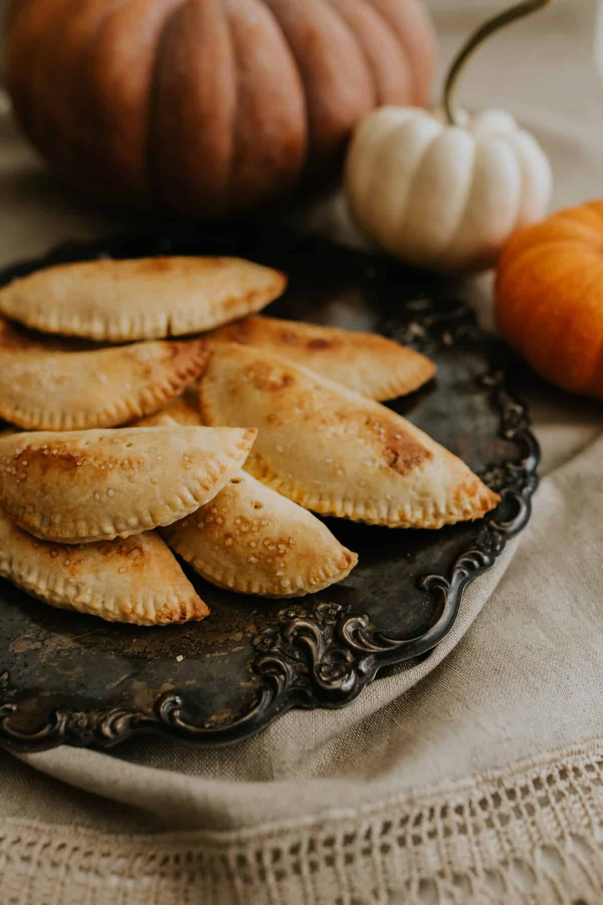 pumpkin empanadas on a vintage silver plate on a brown linen runner with pumpkins in the background