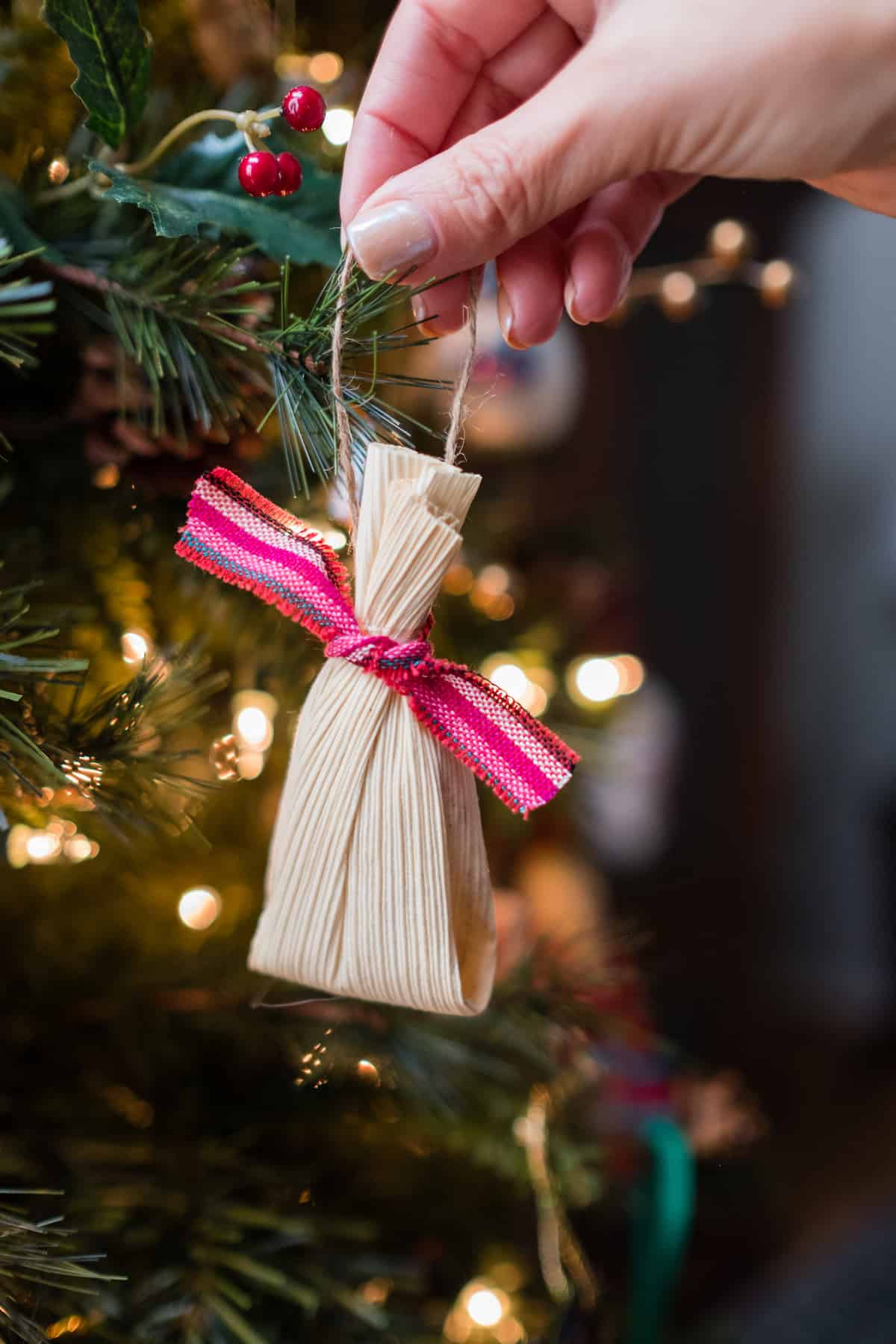 hand hanging a tamale shaped diy christmas ornament on the tree.