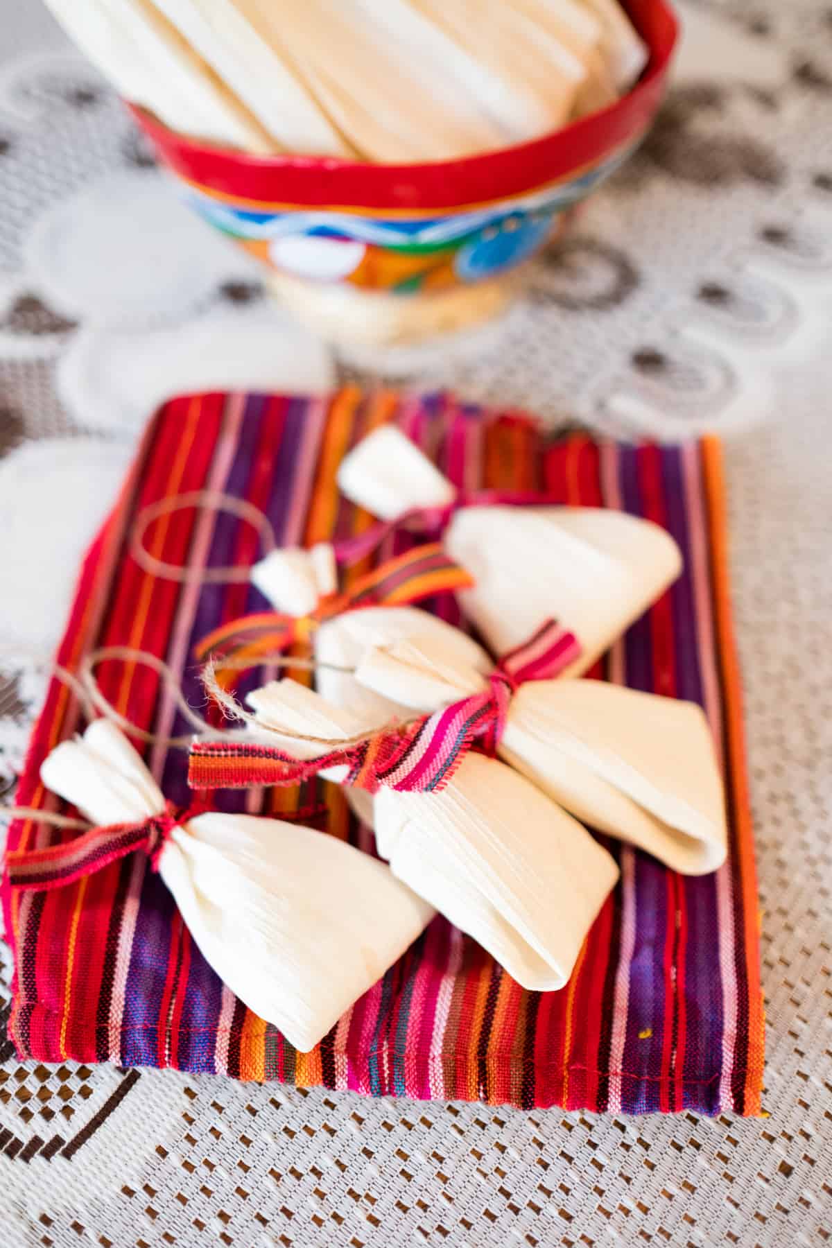 5 mini tamale shaped homemade ornaments on a piece of brightly colored fabric with bits of twine attached for hanging from the tree.