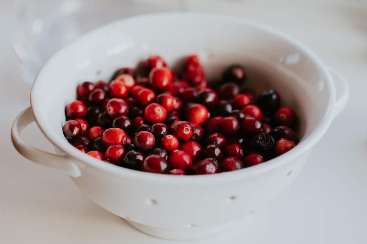 A white colander filled with bright red cranberries to be used in the cranberry puree for this cranberry margarita recipe