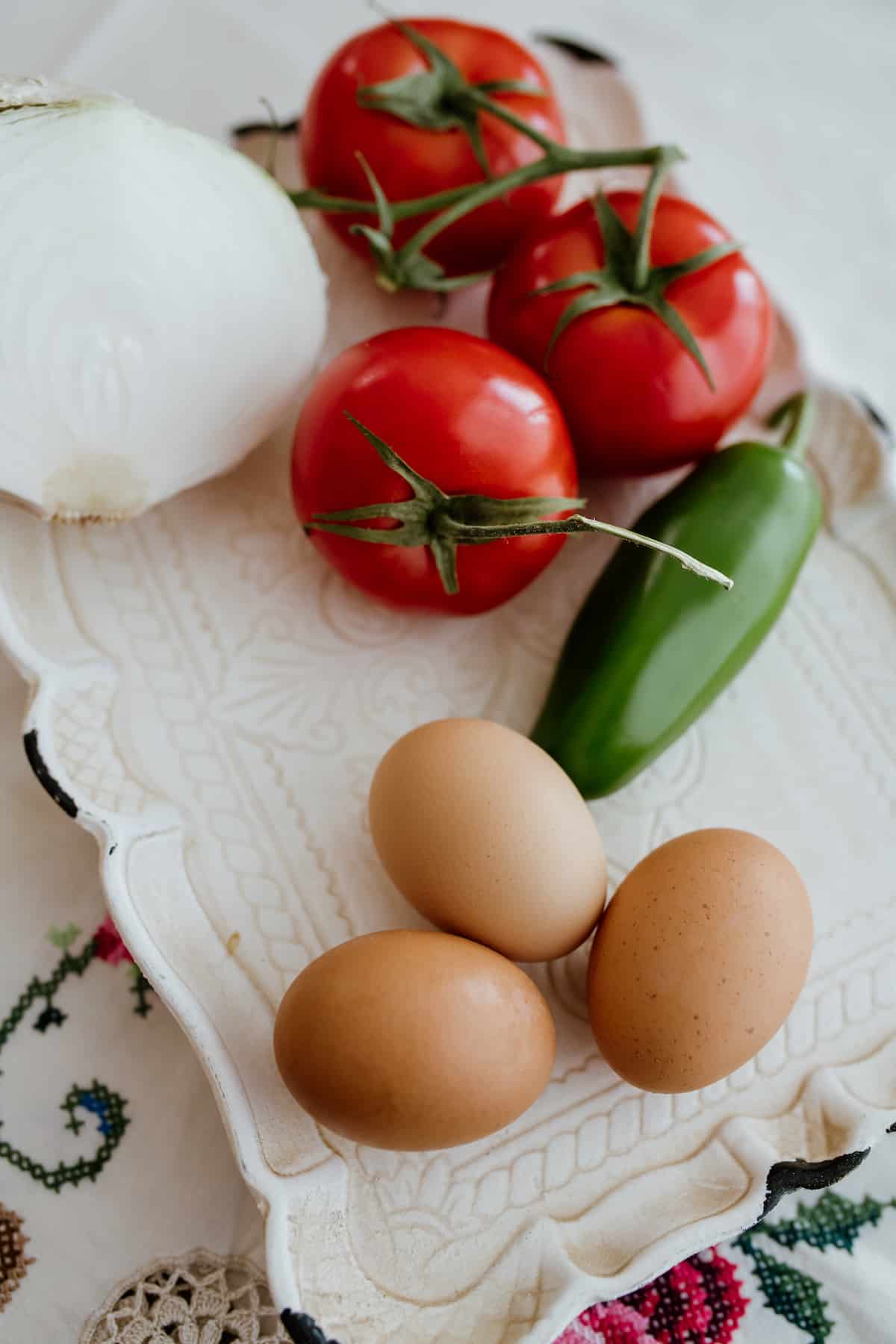 vintage white platter with 3 brown eggs jalapeño and tomatoes on the vine and white onion 
