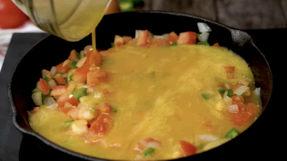 Beaten eggs being poured into a pan with the cooked vegetables to make huevos a la Mexicana.