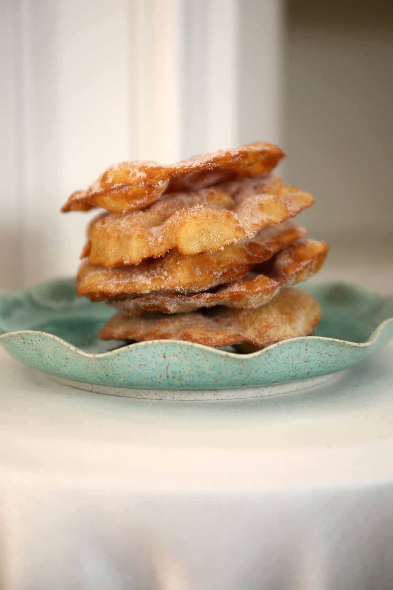 bunuelos sweet Mexican fritters piled high on a ceramic light teal plate.