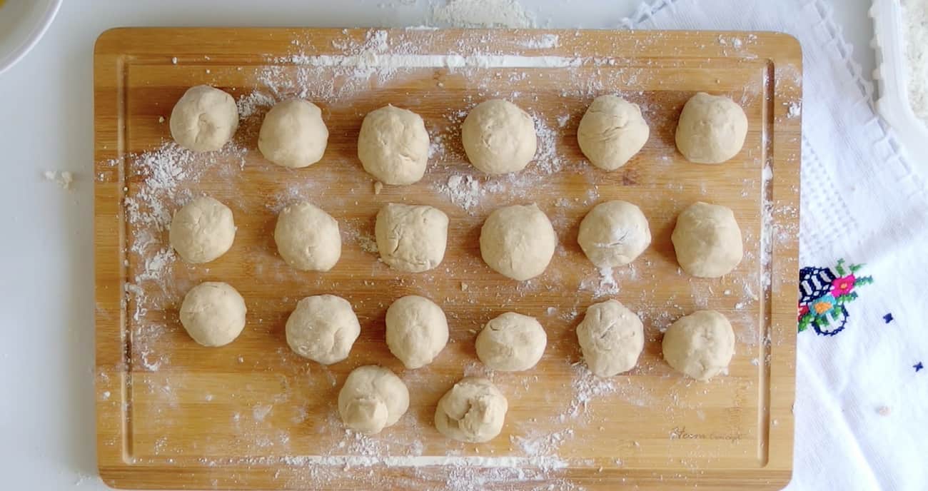 buñuelo dough rolled out into 20 small balls on a wooden cutting board.