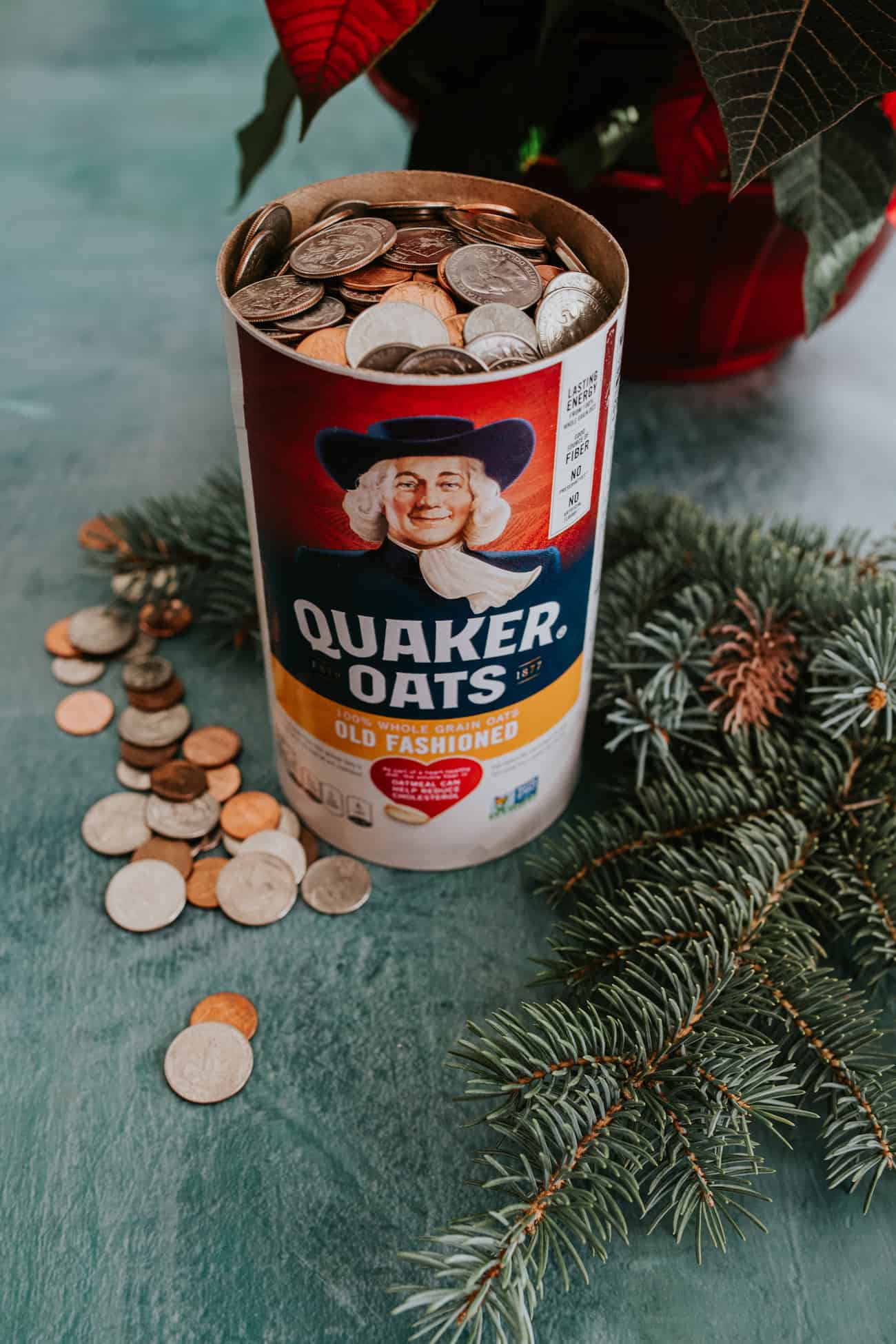 quaker oatmeal canister filled with change on a green table with a sprig of a christmas tree.