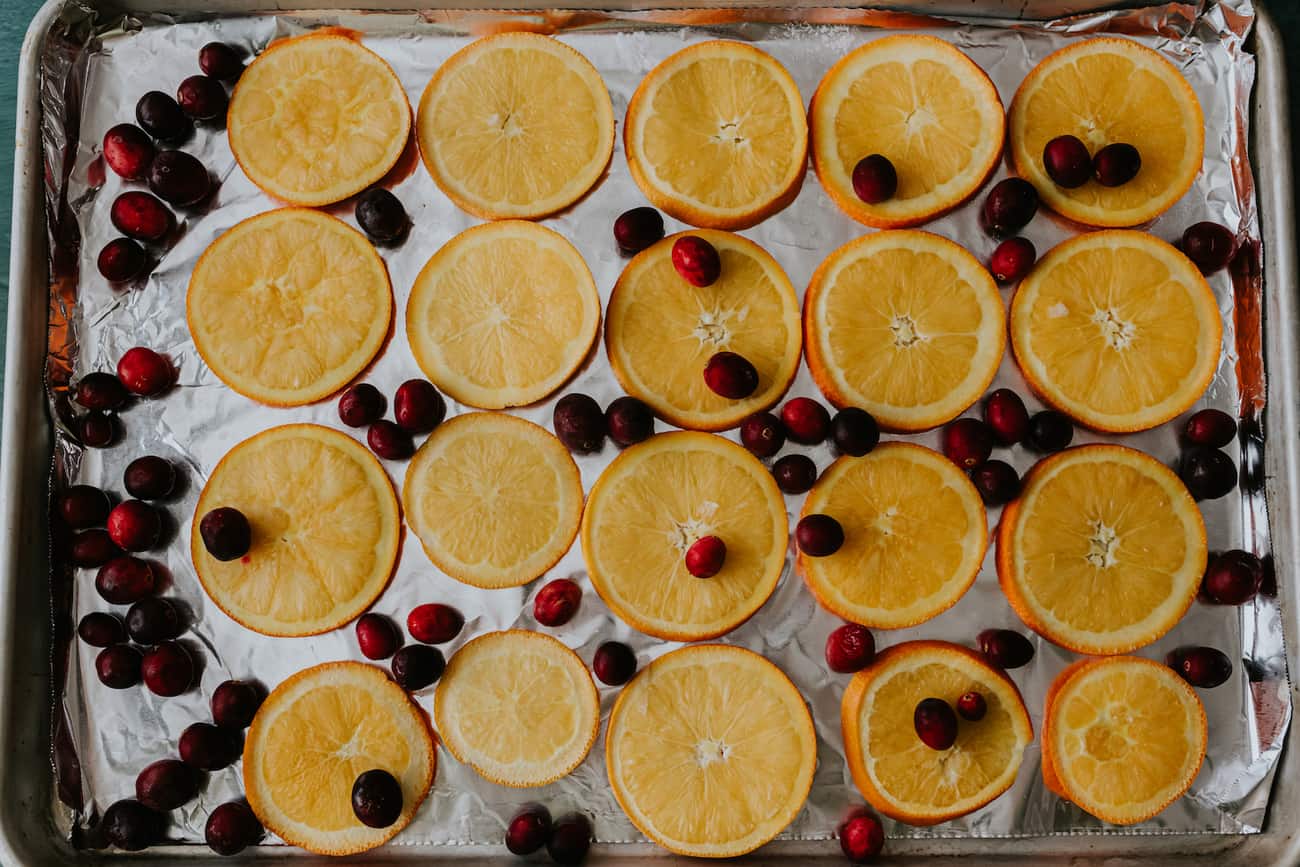 a lined baking sheet filled with a single layer of cranberries and orange slices
