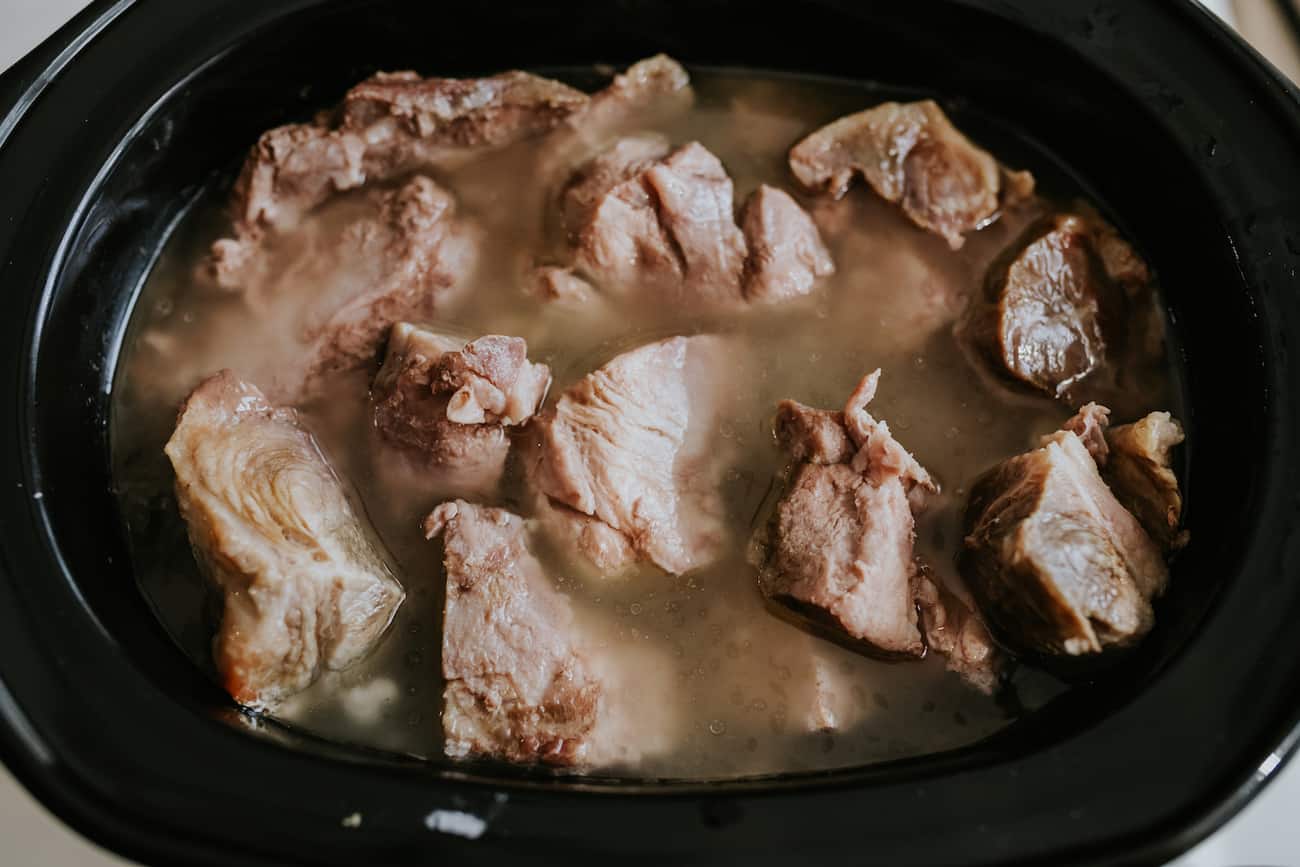 pork butt in a slow cooker with water and spices to make shredded pork for tamales.