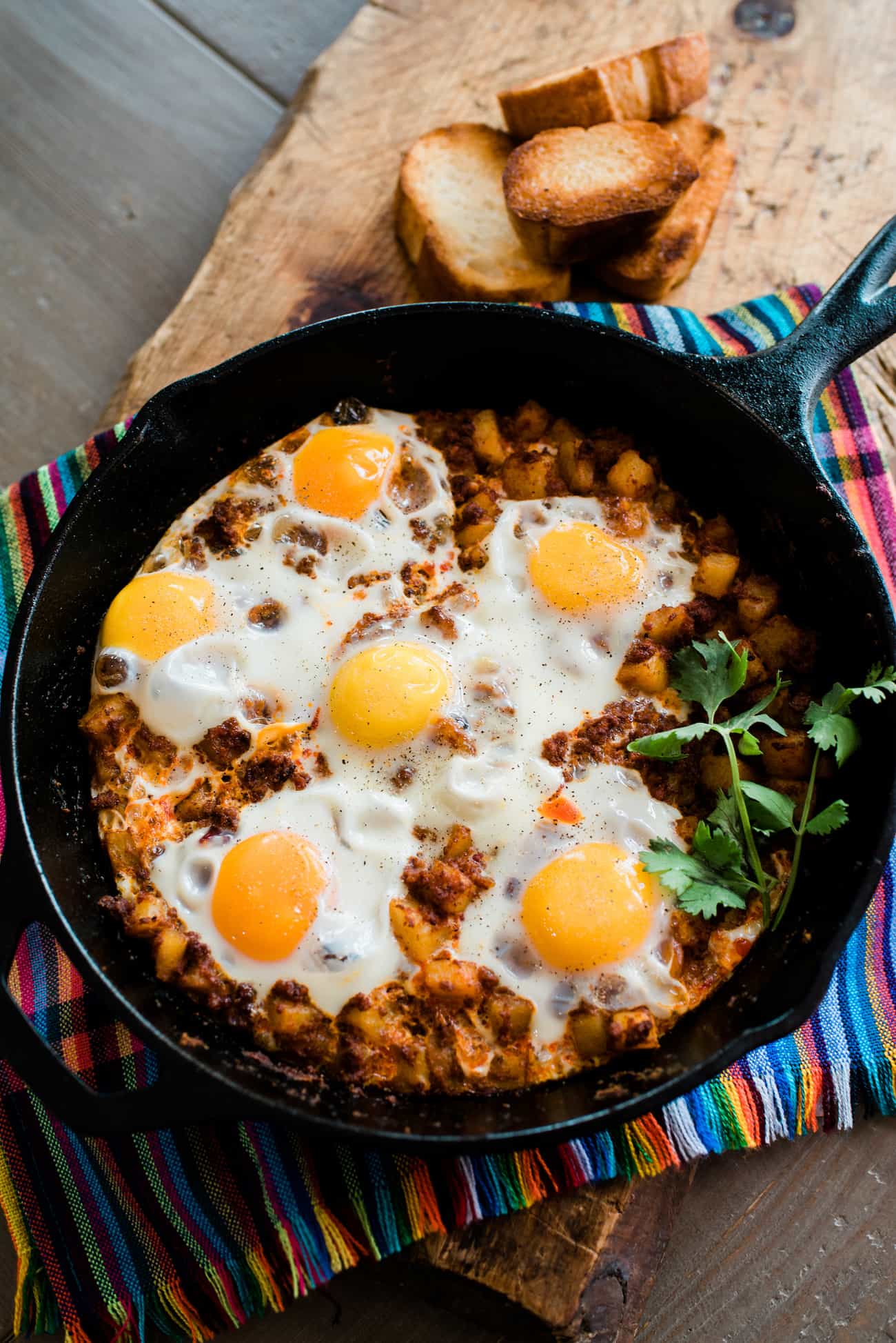 Baked Eggs with Chorizo and Potatoes in an iron skillet on a colorful striped linen.
