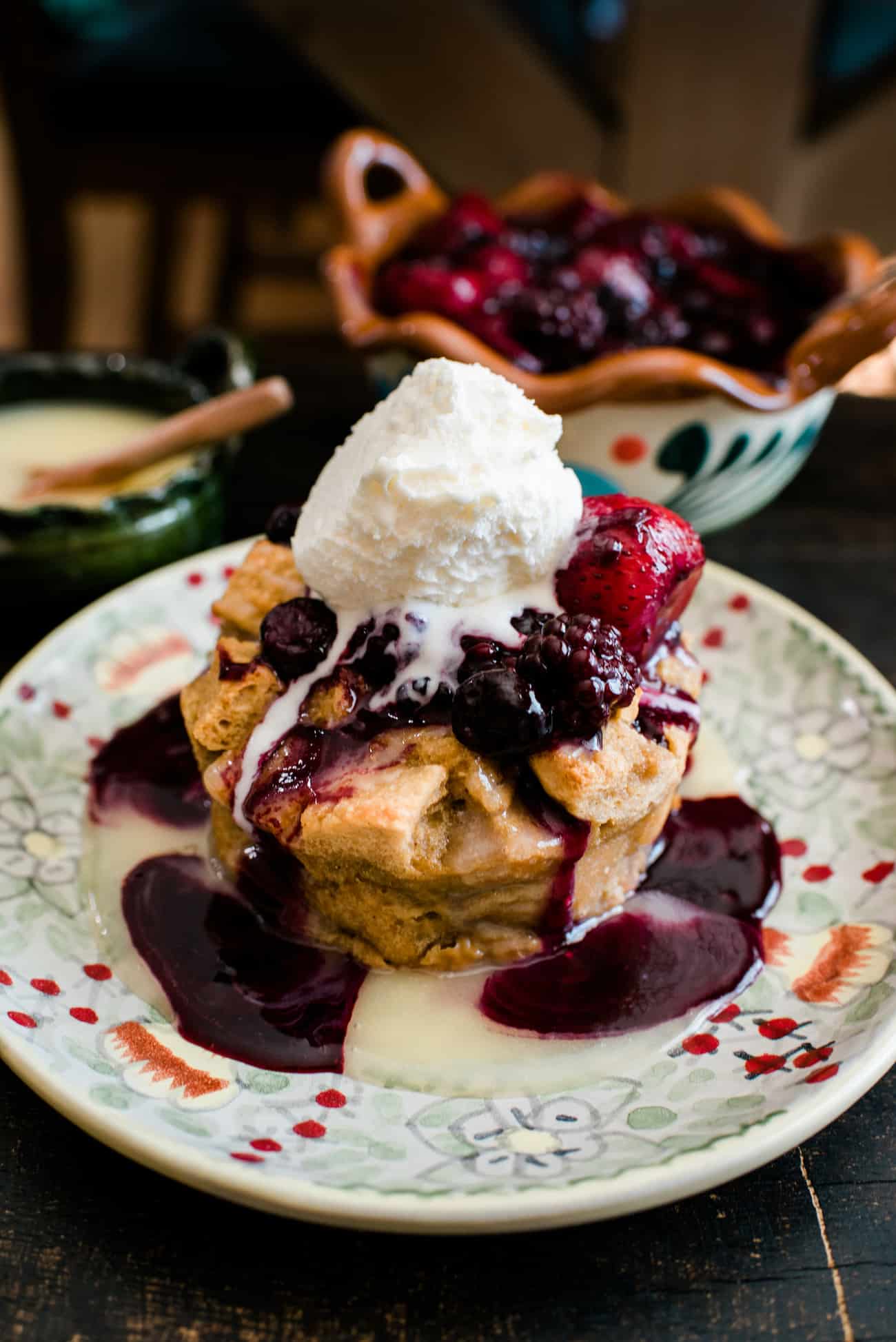 individual bread pudding on a floral plate drizzled with bourbon sauce, berry sauce and topped with a scoop of vanilla ice cream.