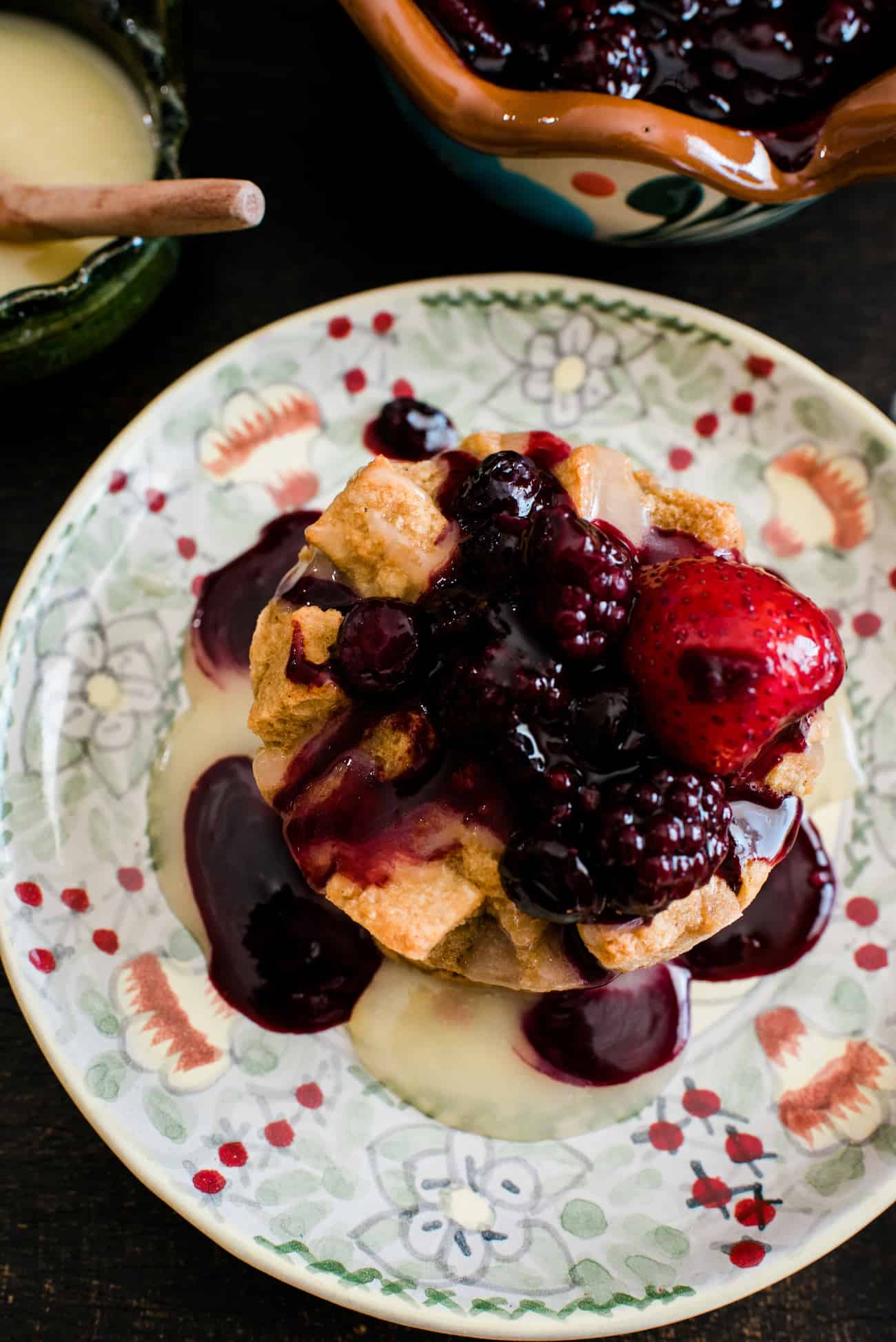 overhead shot of individual bread pudding on a floral plate topped with bourbon sauce and berry sauce.